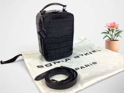 le petit sac noir est posé à côté d'une petite fleur rose