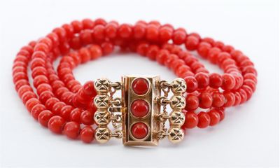 un gros plan sur un bracelet en perles rouges muni d'un fermoir doré