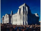 une photo montrant un grand groupe de personnes debout devant un bâtiment recouvert de tissu
