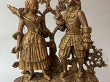 a gold clock with a man and a woman on it