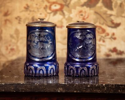 two blue vases sitting on a table with a floral wallpaper behind them