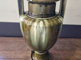 a gold vase on a wooden table with a white wall in the background