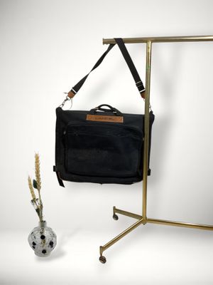 un sac noir accroché à un porte-vêtements à côté d'un vase rempli de fleurs