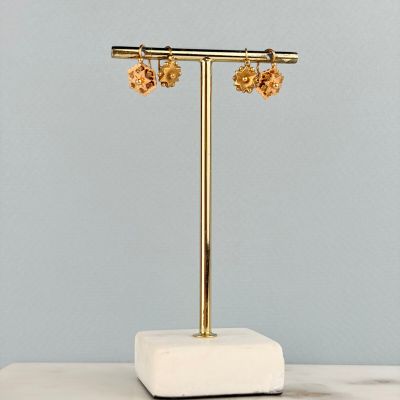 boucles d'oreilles en forme de fleurs dorées posées sur un présentoir posé sur un plan de travail en marbre
