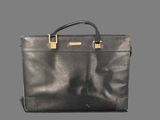 a black leather briefcase with gold handles on a gray background