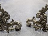 une paire de serre-livres anciens en laiton, ornés de volutes et de feuilles, posés sur un sol en béton