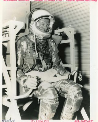 photographie en noir et blanc d'un homme en combinaison spatiale, assis sur une chaise