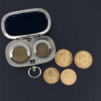 un étui argenté contenant des pièces de monnaie et un porte-clés, posé sur une surface noire