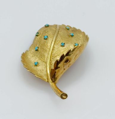 a gold leaf brooch with turquoise stones on it