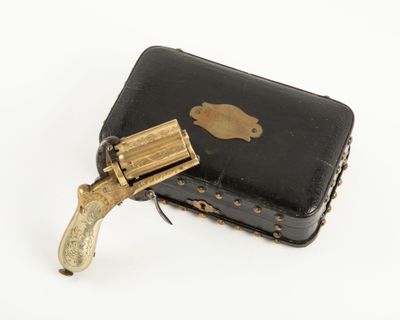 un petit étui noir sur lequel est posé un revolver en laiton
