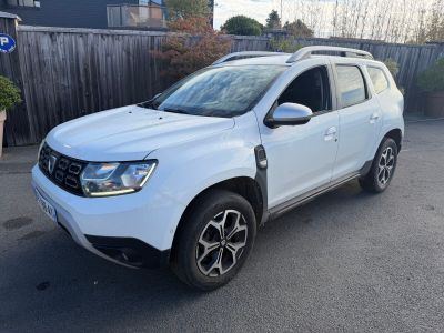 La Dacia blanche est garée devant une clôture en bois.