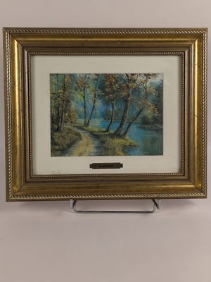 an oil painting of a river and trees in a gold frame on a white wall