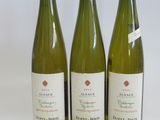three bottles of white wine are lined up on a white surface