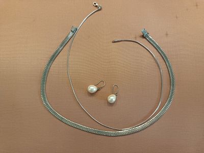a silver necklace and a pair of pearl earrings on a table
