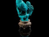 une statue bleue représentant un coq posé sur un rocher, sur fond noir