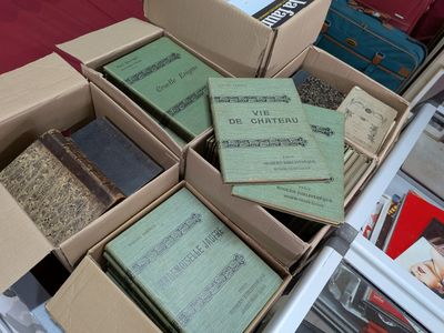 Plusieurs cartons remplis de livres sont empilés sur une table recouverte d'une nappe rouge.