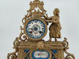 a clock that is sitting on a table with a statue on top of it