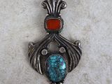 a close up of a turquoise and red stone pendant on a white surface