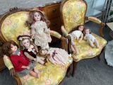 five dolls sitting on a yellow chair in a room
