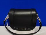 un sac à bandoulière noir posé sur une table blanche, sur fond bleu
