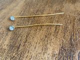two gold - plated hair pins are sitting on a wooden table