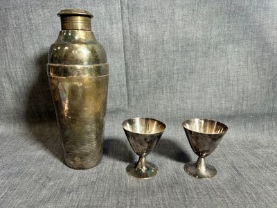 deux vases en argent et une coupe en argent posés sur un tissu gris