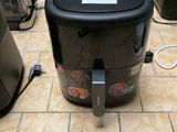 une friteuse à air chaud noire et argentée posée sur un sol carrelé