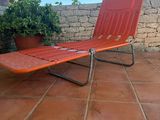 an orange lounge chair sitting on a patio with a potted plant in the background