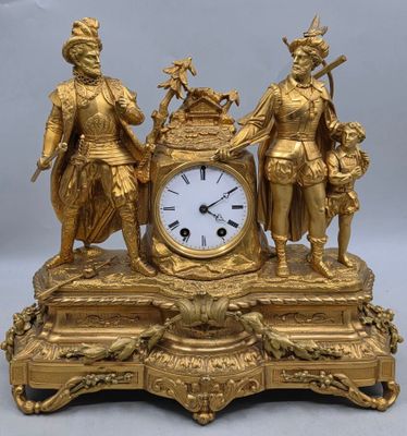 une horloge en or surmontée de trois personnages