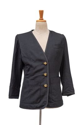 La veste est noire et comporte un bouton doré sur le devant.