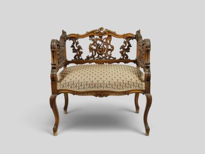 une chaise ancienne sculptée, dont l'assise est recouverte d'un tissu beige