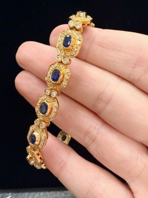 un gros plan d'une personne tenant un bracelet en or orné de pierres bleues