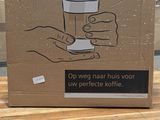 une boîte en carton posée sur une table, avec une main tenant une tasse de café