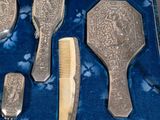 a blue velvet case with a silver set of hair brushes and combs in it