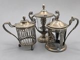 two silver plated teapots and a glass teapot on a table