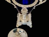 an antique silver and blue glass cup on a stand on a black background