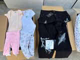 several pairs of baby clothes are in a cardboard box on the ground