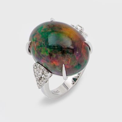 une image représentant une bague ornée d'une pierre noire et verte, entourée de diamants blancs