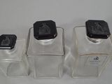 three clear glass containers with black lids on a white surface