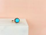 a gold ring with a turquoise stone sits on a marble block