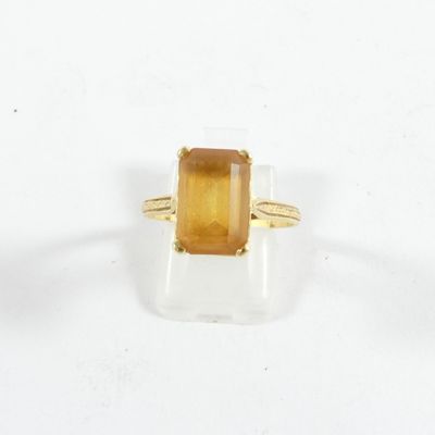 un gros plan d'une bague ornée d'une pierre jaune sur un fond blanc