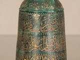 a green and gold bell with arabic writing on it