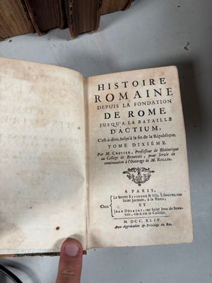 Quelqu'un tient un vieux livre ouvert sur une table, à côté d'une pile de livres.