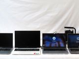 Quatre ordinateurs portables sont alignés sur une table devant un fond blanc.