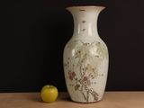 a white vase with a painting on it next to an apple