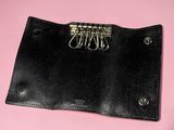 black leather wallet with five metal clips attached to it on a pink background