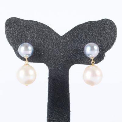 une paire de boucles d'oreilles en perles et en or, posée sur un socle noir
