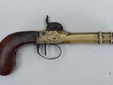 un vieux revolver en laiton avec une crosse en bois, posé sur une surface blanche