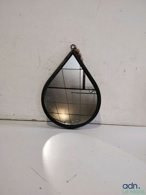 un miroir noir en forme de larme posé sur un comptoir blanc