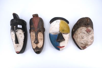 quatre masques en bois sont alignés sur une surface blanche